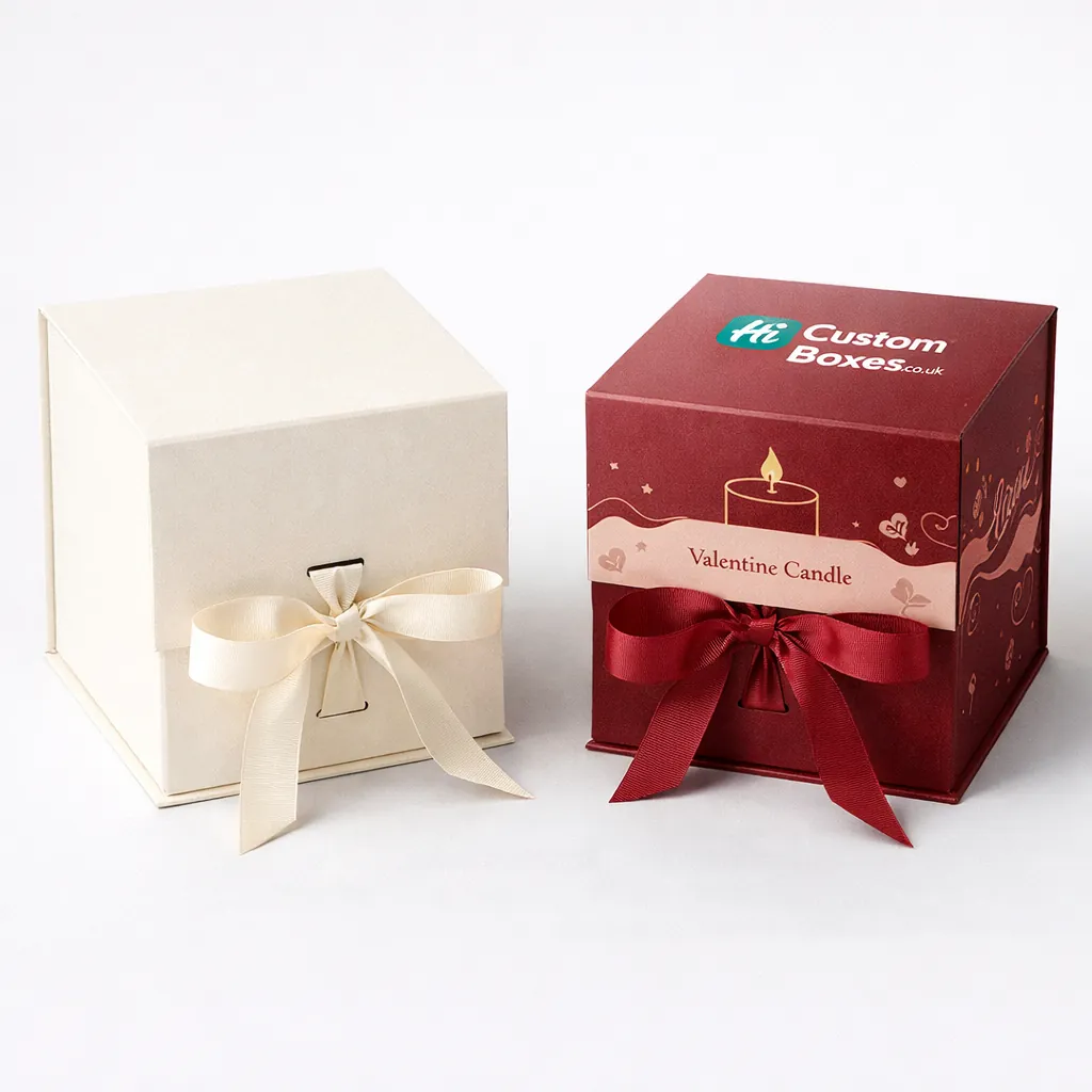 Two elegant square gift boxes, one ivory and one maroon, featuring decorative satin bows and candles. class=